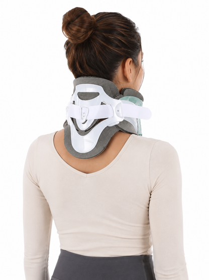 A woman viewed from the back wearing a white and gray cervical neck brace on her neck, against a plain white background.